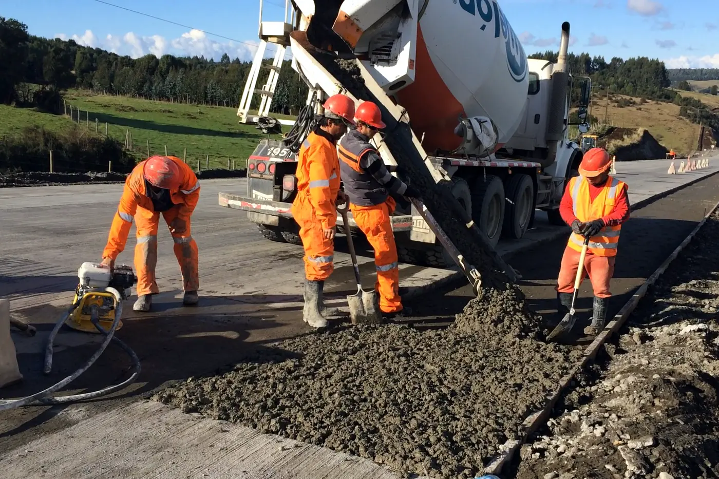 La cuadrilla completa extendiendo el hormigón de una calzada de camino, con el camión mixer descargando detrás