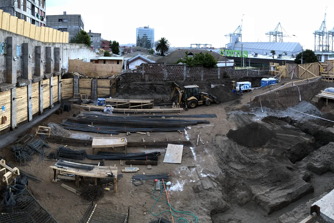 Excavación profunda para las fundaciones de un edificio, con el muro de sostenimiento y la ciudad asomando arriba