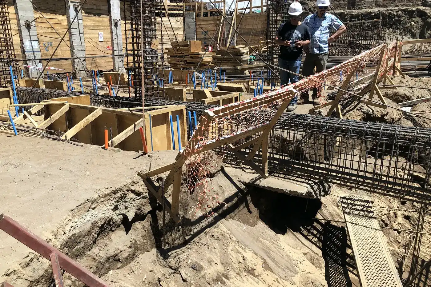Dos trabajadores con casco recorriendo la obra gruesa dentro de la excavación