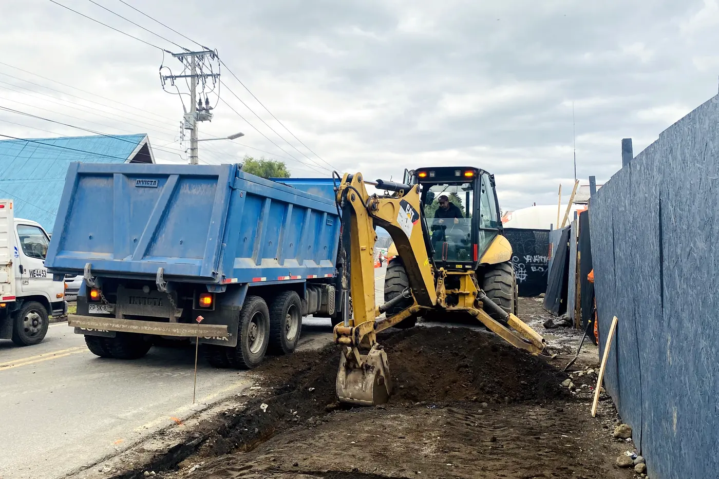 Retroexcavadora cargando un camión tolva en un tramo de calle cortado y señalizado