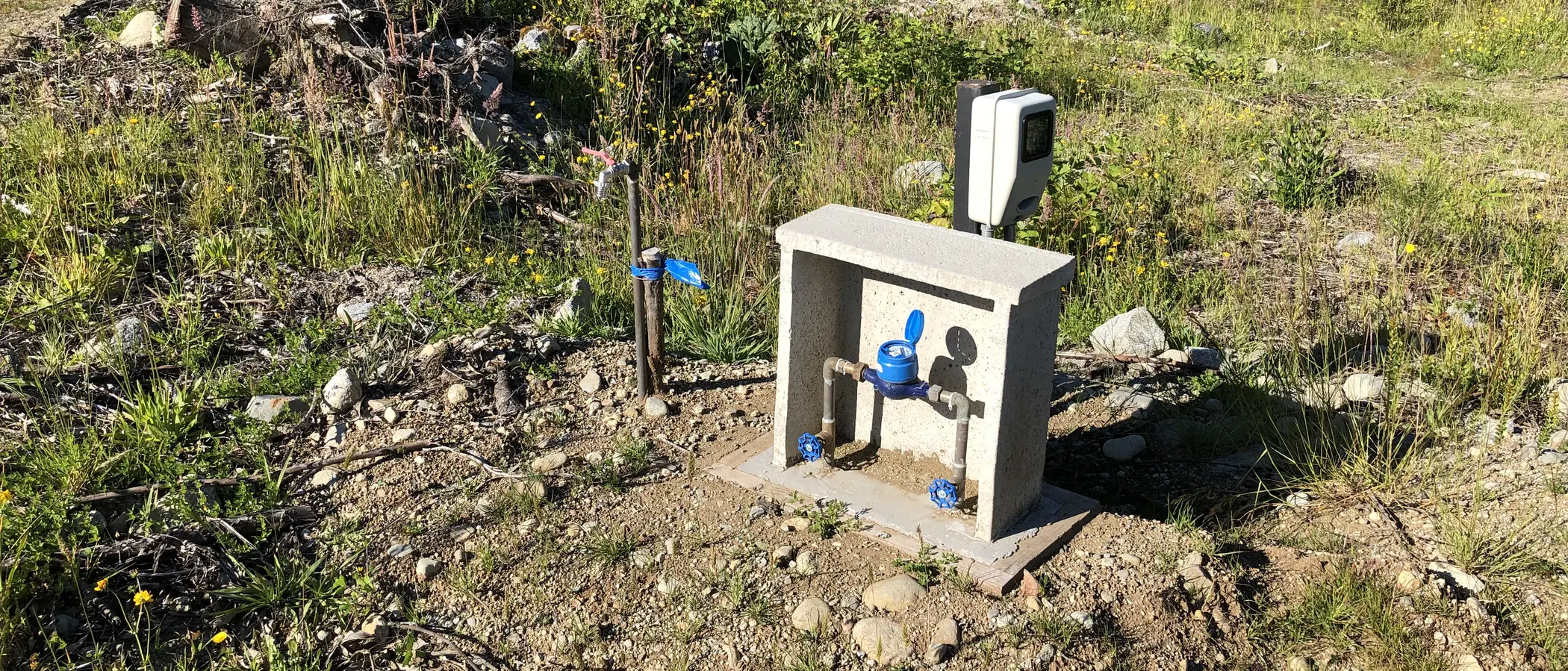 Arranque de agua potable terminado en un predio rural del sur: nicho de hormigón con medidor y llaves de paso, sobre terreno recién intervenido