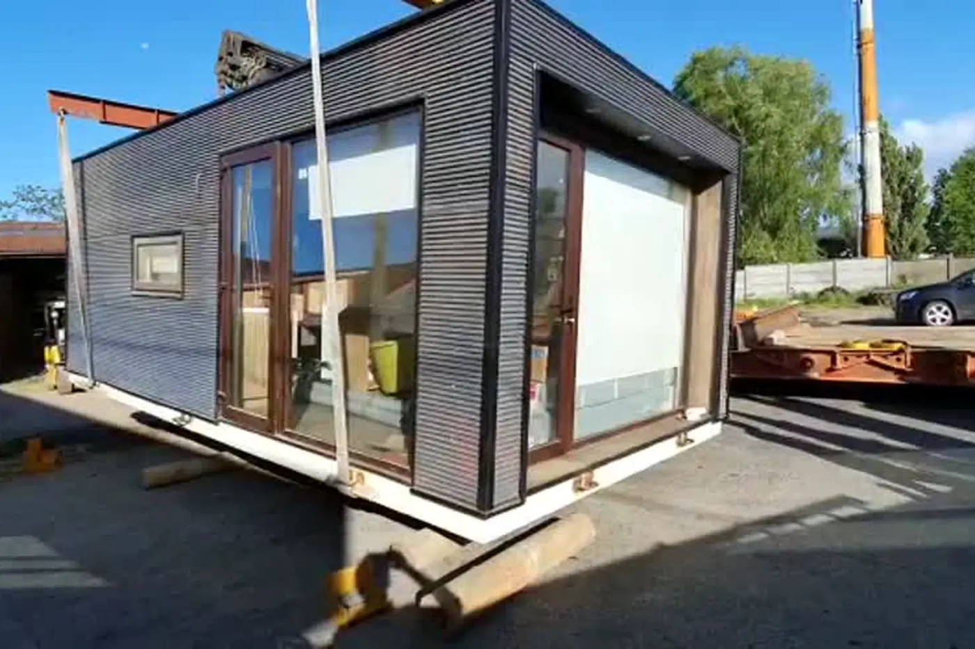 La Tiny House terminada, apoyada en el suelo: revestimiento vertical oscuro y ventanales de piso a cielo